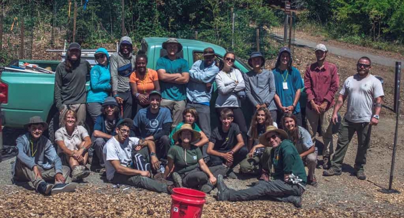 A group of outward bound students stand in front of a green truck and pose for a photo during a service day